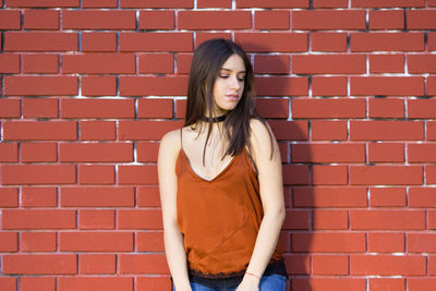 Young woman standing against brick wall