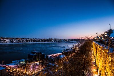 Illuminated city by sea against clear blue sky at night