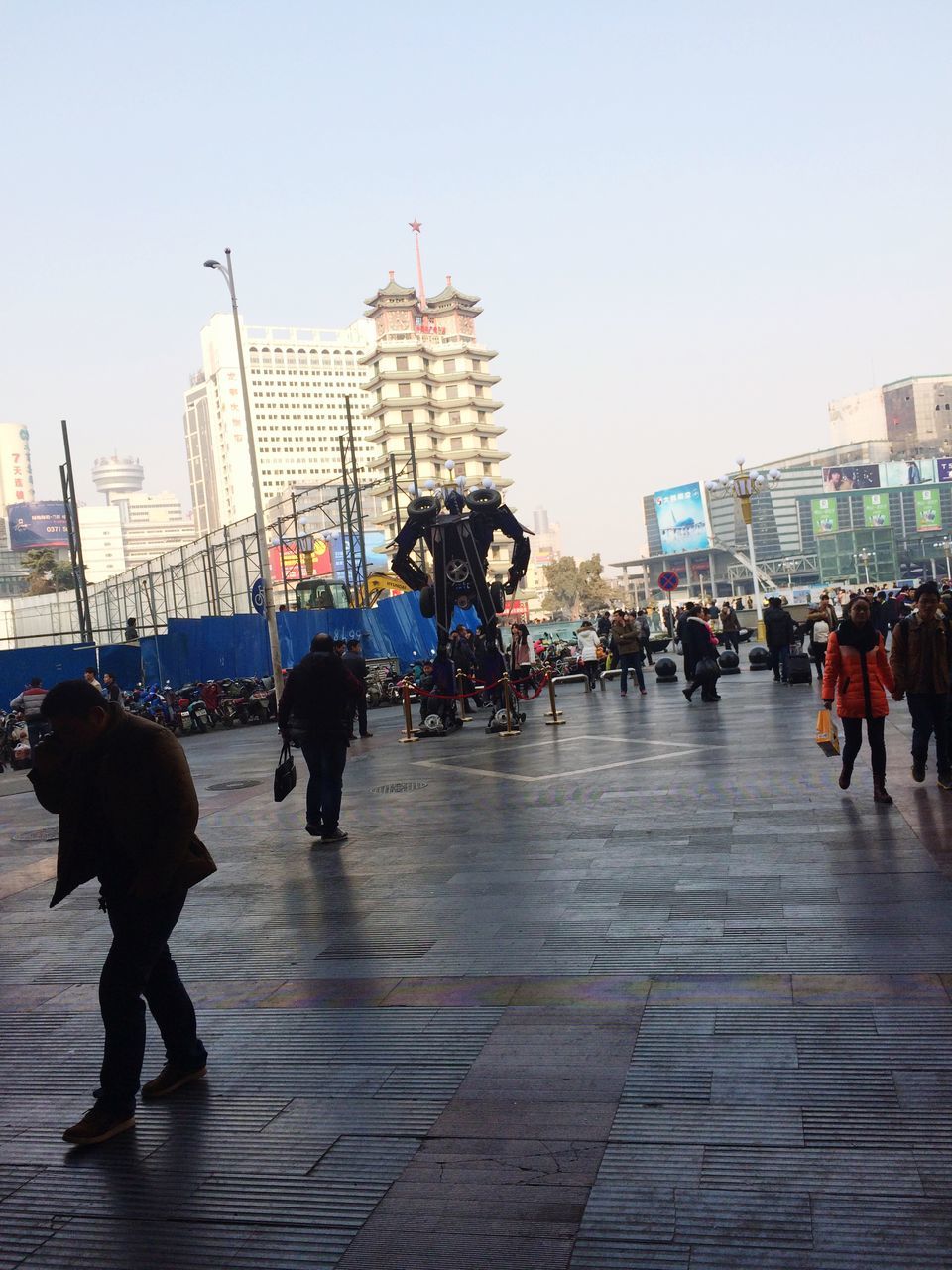 building exterior, architecture, large group of people, walking, built structure, men, city, person, lifestyles, city life, street, leisure activity, full length, clear sky, mixed age range, city street, sidewalk, medium group of people, sky