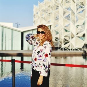 Woman wearing sunglasses standing by railing against water