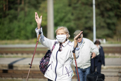 A group of senior travelers with masks on their faces cross the railway tracks