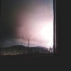 Silhouette buildings seen through wet glass window