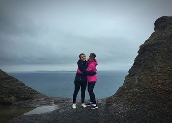 Mother and daughter embracing while standing on cliffs of moher against cloudy sky