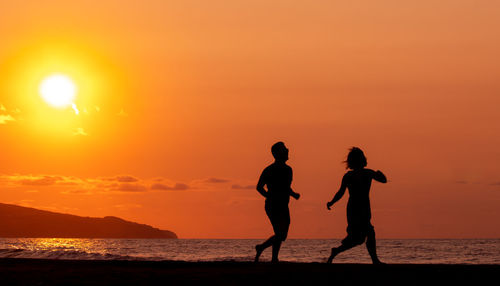 Couple running and having fun at beach, silhouette in sunset, love and friendship.