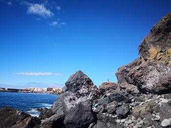 Rock formations by sea against blue sky