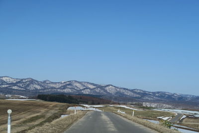 Road leading towards mountains against clear blue sky