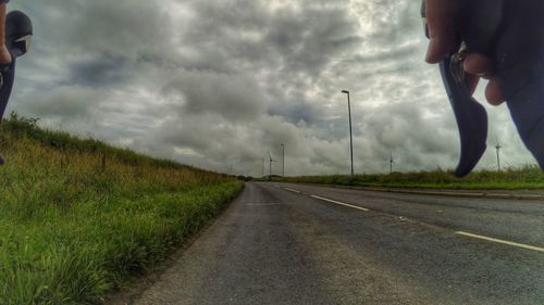 Low section of man on road against cloudy sky
