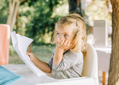 Girl holding paper looking away while sitting on high chair