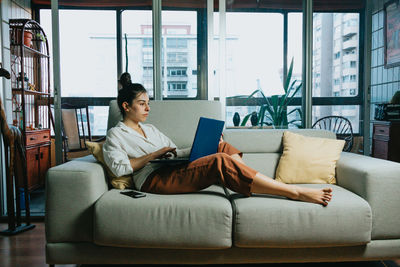 Woman using laptop while sitting on sofa at home