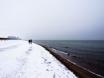 People walking on snow covered beach against sky