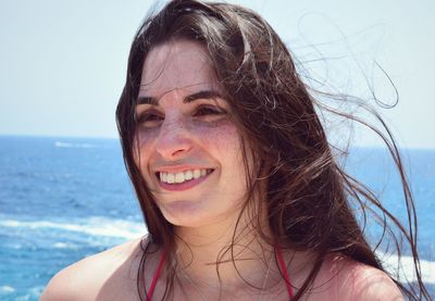 Close-up portrait of smiling young woman against sea