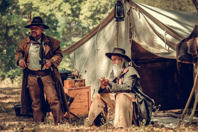 Men sitting on land against tent in forest