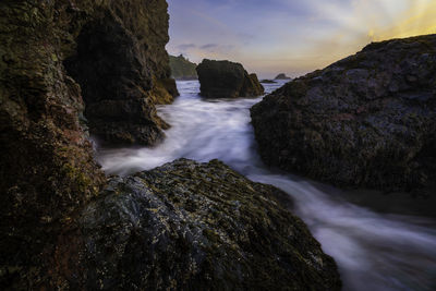 Scenic view of waterfall by rocks against sky