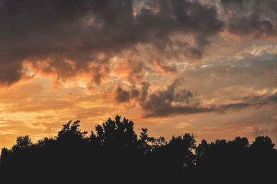 Low angle view of silhouette trees against dramatic sky