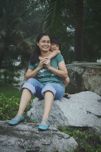 Portrait of smiling young woman sitting on tree trunk