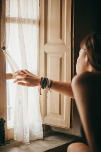 Woman touching curtain while looking through window