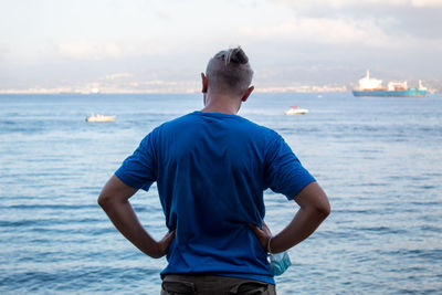 Rear view of man standing in sea against sky