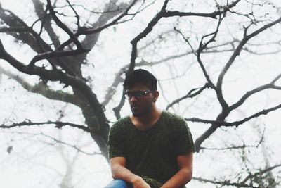 Portrait of young man standing against bare tree