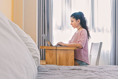 Side view of young woman sitting on table at home