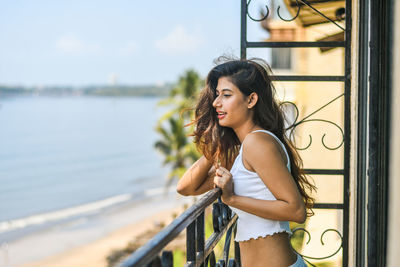 Smiling young woman looking away while leaning on railing