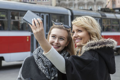 Portrait of smiling young woman using mobile phone in city