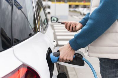 Man using smart phone and charging electric car at station