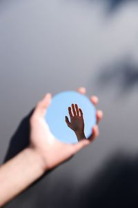 Reflection of hand against sky in mirror