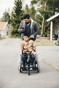 Father using smart phone while pushing autistic son on wheelchair