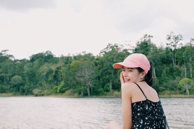 Portrait of young woman against lake and trees against sky