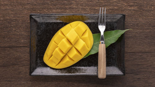 Tasty fresh yellow ripe mango with fork and mango leaf in rectangular ceramic plate on rustic wood