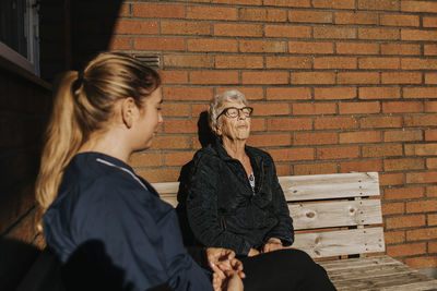 Home caretaker and senior woman sitting on bench and sunbathing