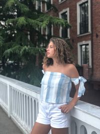 Young woman looking away while standing against building