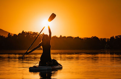 Silhouette man standing by lake against orange sky