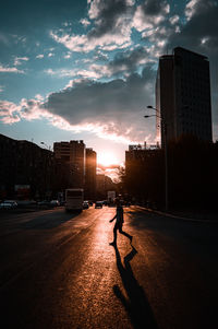 Man on street amidst buildings against sky during sunset