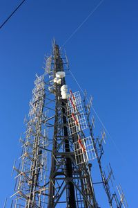 Low angle view of communications tower against clear blue sky