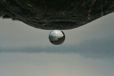 Close-up of drop falling on water against sky