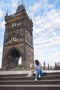 Woman sitting with dog on steps against historical building