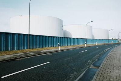 Road by fuel storage tank against sky