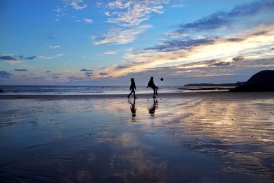 Silhouette people on beach against sky during sunset