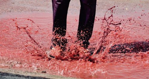 Low section of man jumping on red puddle during holi