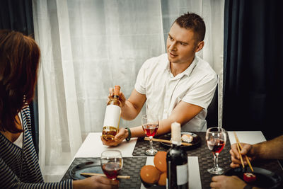 Man showing wine bottle to friends while sitting at restaurant
