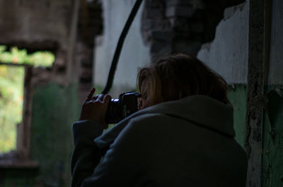 Rear view of woman photographing with digital camera at abandoned building