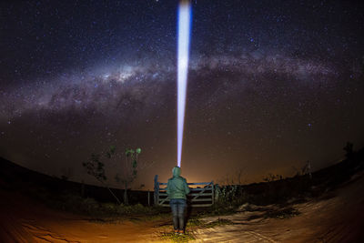 Rear view of woman with illuminated flashlight standing against star field at night