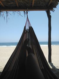 Low section of woman in hammock at beach against sky