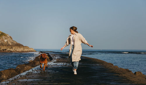 Full length of young woman standing on beach against clear sky