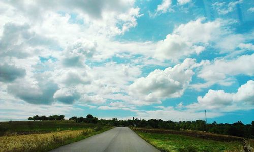 Road passing through field against cloudy sky