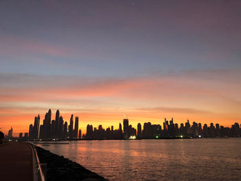 Sea by buildings against sky during sunset