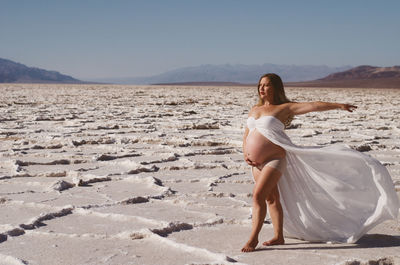 Pregnant woman with arms outstretched standing on field against sky