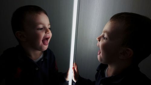  cute boy sticking out tongue while looking in mirror at home