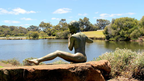 Statue by lake against sky